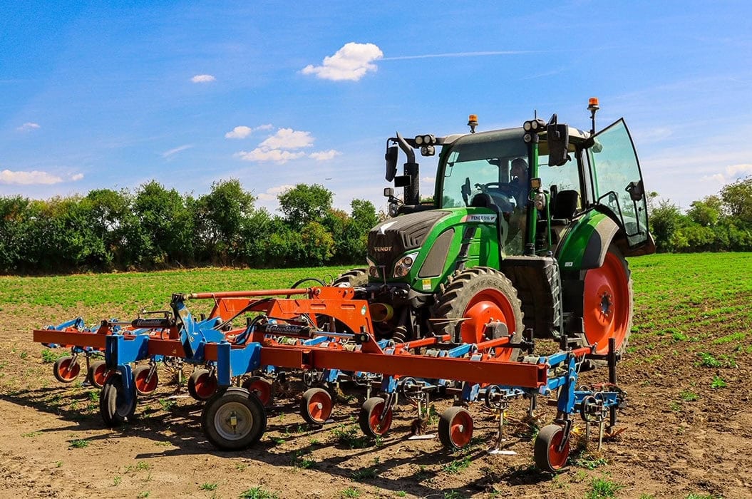 Ein grüner Traktor auf einem Feld mit blauen und orangefarbenen Landwirtschaftsgeräten.